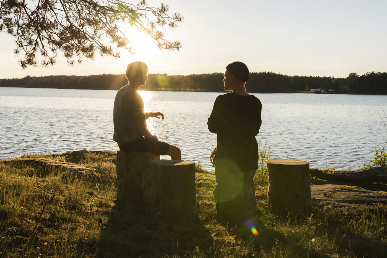 Deux hommes échangent au bord d’un lac, dans la lumière du soir.